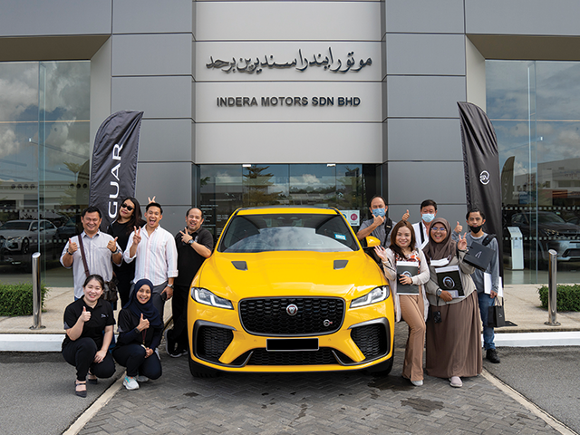 A group of people comprising of members of the media smile at the camera as they post in front of Jaguar F-PACE SVR in Sorrento Yellow