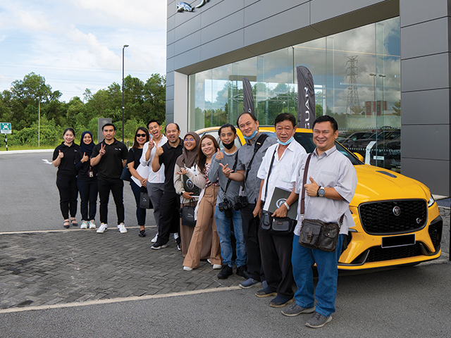 A group of people comprising of members of the media smile at the camera as they post in front of Jaguar F-PACE SVR in Sorrento Yellow